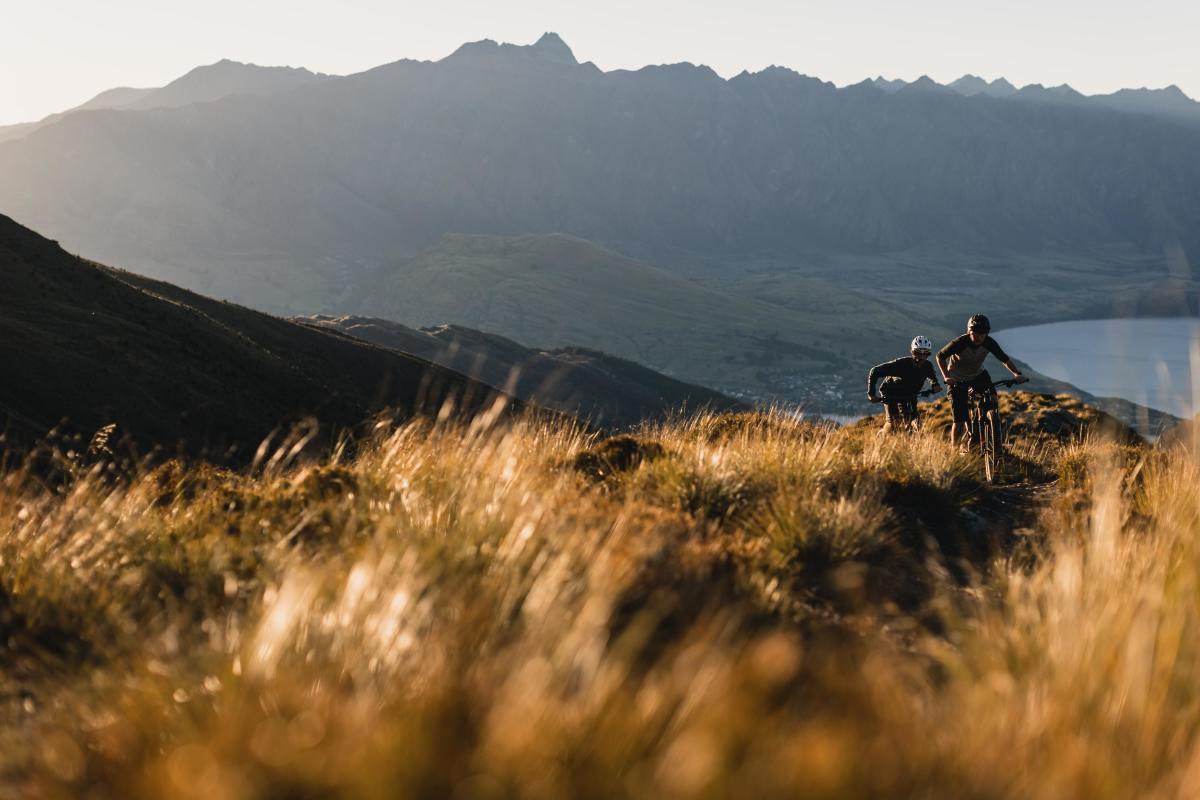 Two riders climbing a golden tussock ridge at sunset